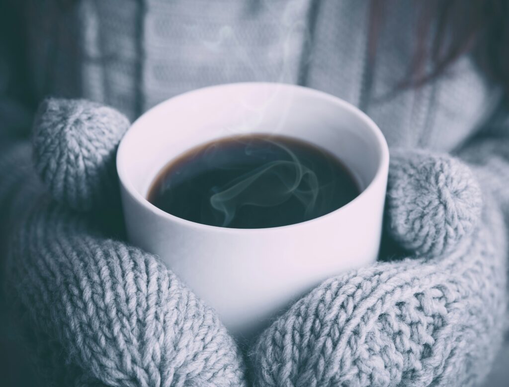 rykande kopp kaffe med varma vantar som håller om den